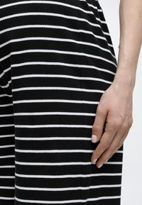 Δεξί χέρι που ακουμπά σε υφάσμα με οριζόντιες μαύρες και άσπρες ρίγες, κοντινό πλάνο που δείχνει υφή και φυσικούς τόνους δέρματος.