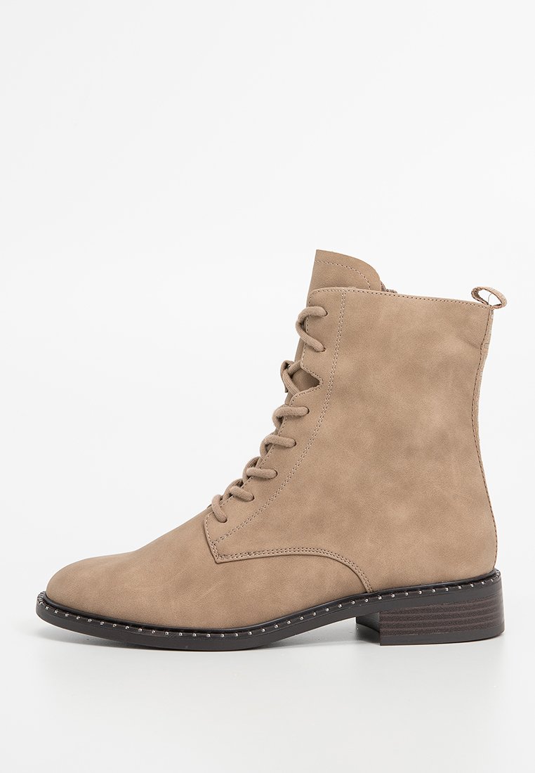 Tannfarbene Ankle Boots mit glattem Synthetik-Obermaterial, Schnürdesign, abgerundeter Zehenpartie und strukturiertem Schuhsohle mit kleinen Nietenakzenten. Flacher Absatz.