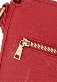 Borsa a tracolla in pelle rossa con superficie texturizzata, motivi impressi e dettagli in oro con una charm. Design compatto con chiusura sicura.