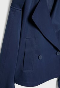 Granatowa podwójnie zapinana marynarka z dużymi klapami, teksturowana tkanina, zapinana na dwa guziki, z boczną kieszenią. Widoczne czyste detale szwów.