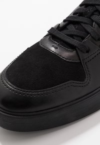 Czarny sneaker wykonany z połączenia gładkiej skóry i zamszu, z okrągłym noskiem, teksturowanymi sznurowadłami oraz wzmocnionymi detalami szwów.