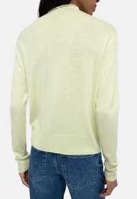 Jasnożółty sweter dziany o luźnym kroju, z długimi rękawami i prążkowanymi mankietami. Tył ma gładką teksturę i prosty design.