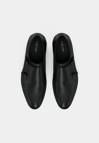 Μαύρες δερμάτινες παπούτσια με κομψό σχέδιο, στρογγυλεμένες μύτες και δύο ρυθμιζόμενες πόρπες στα πλάγια. Λείο υλικό και ελάχιστες λεπτομέρειες.