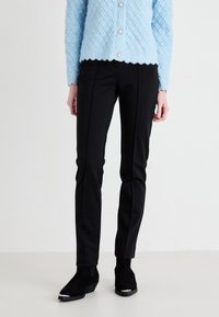 Black tailored pants with a slim fit and front seam detailing, paired with a light blue textured cardigan and black ankle boots.