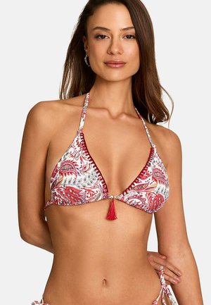 Femme portant un haut de bikini halter rouge et blanc à motif cachemire avec détail de pompon, posant avec une main dans le dos.