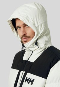 Giacca a vento bianca e nera con cappuccio, dotata di zip, caratterizzata da un design color block, cappuccio regolabile con cordino elastico e un logo ben visibile sul davanti.