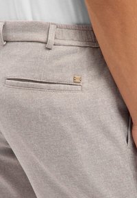 Beżowe spodnie o fakturze, z tylną kieszenią ze szwem i małym metalowym zdobieniem. Zaprojektowane z luźnym krojem.