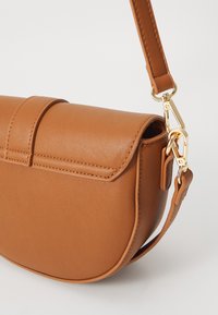 Hnědá koženková crossbody taška zaobleného tvaru, s magnetickým uzávěrem a zlatými detaily na popruhu.
