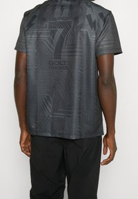 Černé sportovní tričko s geometrickým vzorem, které má různé textury, designy a akcenty v podobě blesků na zadní straně.