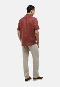 Chemise à manches courtes couleur rouille en tissu léger, associée à un pantalon beige clair et des baskets marron, vue de dos.