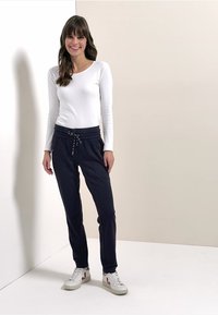 Top blanco de manga larga combinado con pantalones jogger azul marino con cintura elástica y cordón. Modelo con zapatillas blancas.