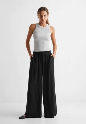 Sivý bezrukávový top s okrúhlym výstrihom, ktorý je skombinovaný s voľnými čiernymi nohavicami s širokými nohavicami, elastickým pásom a bočnými vreckami.