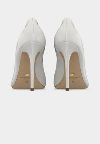 Weiße High Heels aus Lackleder mit spitzer Zehenpartie, 10 cm Stiletto-Absatz und glatter Oberfläche. Goldene Markenkennzeichnung auf der Innensohle sichtbar.