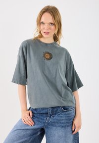 Jasnoszary, oversize bawełniany T-shirt z haftowanym wzorem słońca i księżyca na piersi. Krótkie rękawy i luźny krój.