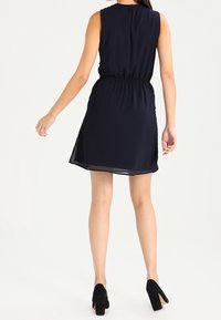 Námorně modré bezramínkové šaty se staženým pasem, lemem do tvaru A a průhlednou tkaninou. V kombinaci s černými lodičkami na vysokém podpatku. Jednoduchý design na zádech.