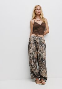 Top corto a costine marrone con bordino in pizzo abbinato a pantaloni larghi con motivo camouflage, dotati di una vita con cordoncino e tasche laterali. Sandali completano il look.