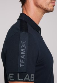 Granatowa koszulka polo z fakturowanym kołnierzykiem, z kontrastowymi graficznymi akcentami na rękawach. Klasyczny krój z krótkimi rękawami.