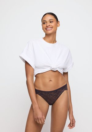 Witte geknoopte crop t-shirt met korte mouwen, gecombineerd met donkere kant stringonderbroek, met een ingewikkelde kantstructuur en een getailleerd ontwerp.