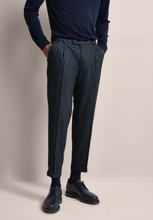 Tailored dark gray trousers with a textured fabric, pleated front, and cuffed hems, paired with dark shoes and a navy sweater.