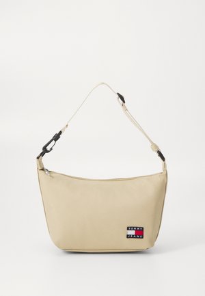 Bolso de hombro de nylon beige con forma curva, cierre de cremallera y correa ajustable. Presenta un parche con el logotipo en tonos rojo, blanco y azul.
