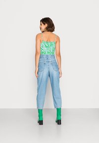 Top verde cortado com padrão abstrato branco, combinado com jeans de cintura alta azul claro e botas verdes de salto, visto de costas.