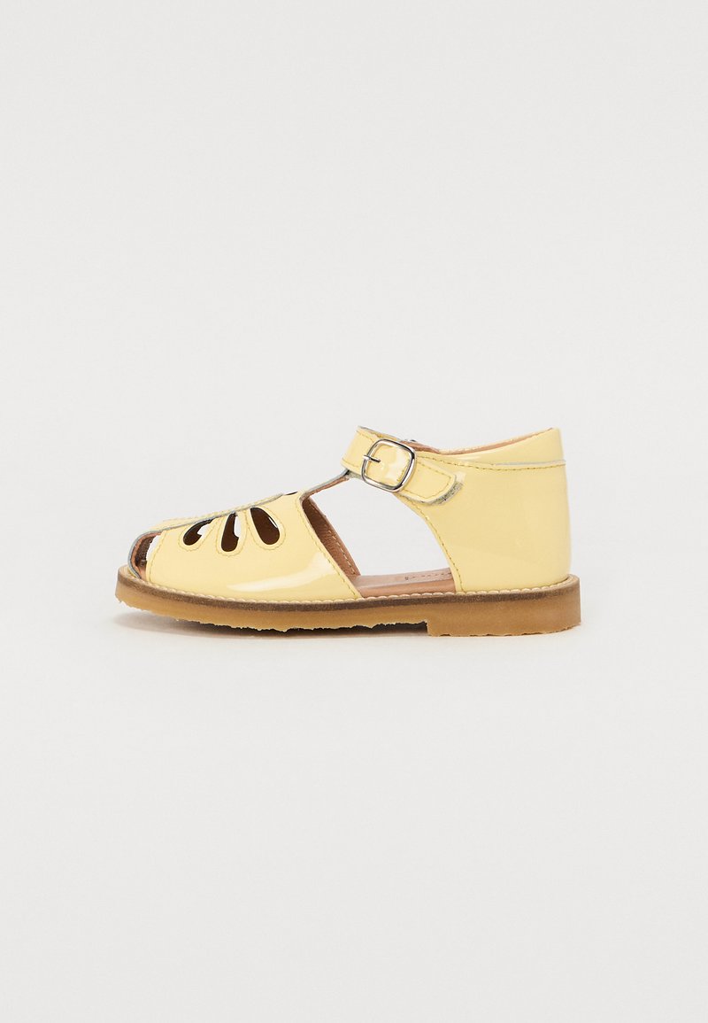 Sandal de verniz amarelo com designs recortados, fecho de fivela e sola plana de borracha. Design de biqueira aberta e tira traseira.