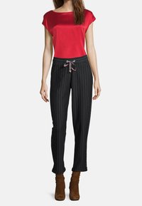 Röd satin topp med korta ärmar i kombination med svarta byxor med ränder och resårmidja samt uppvikta fållar. Ljusbruna ankelskootar fulländar outfiten.