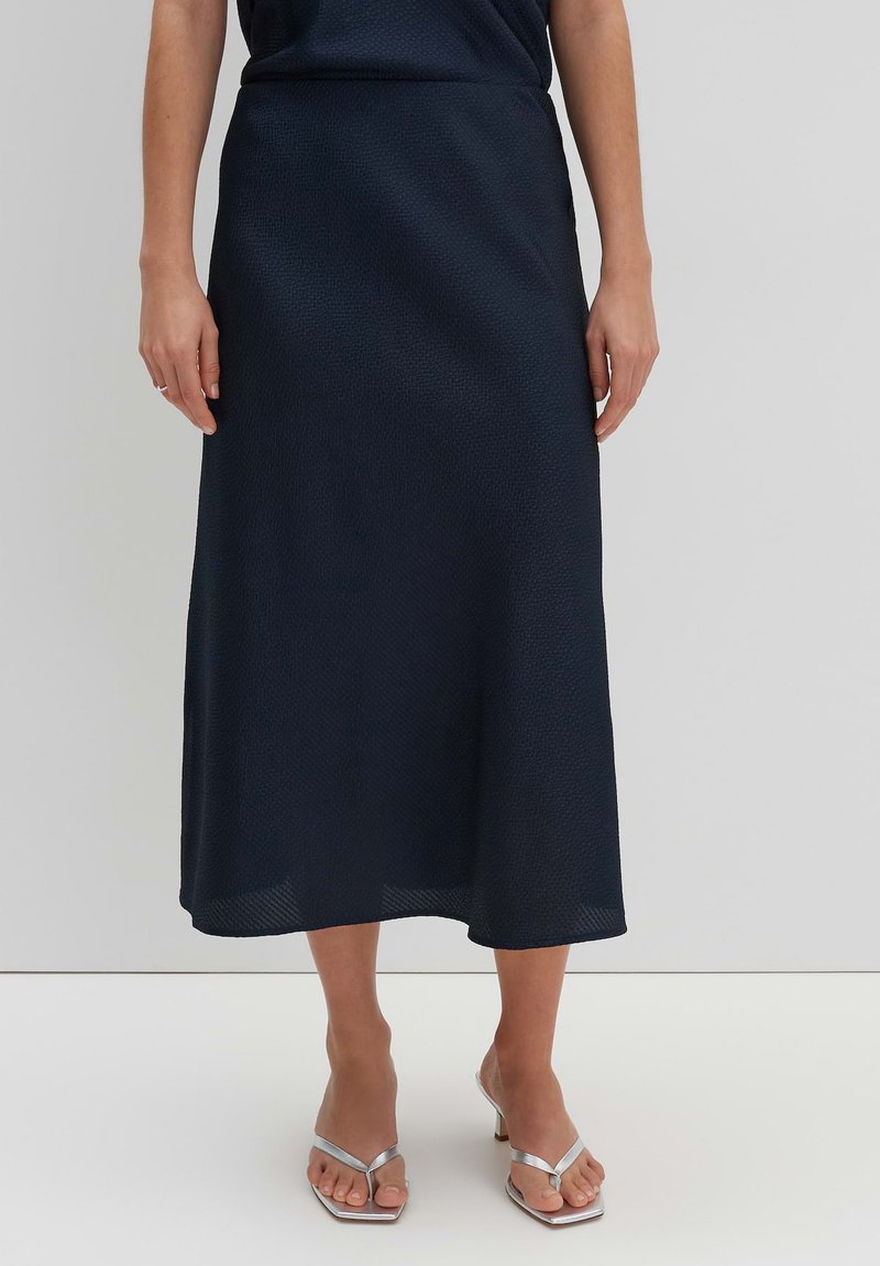 Marineblaue Midiskirt mit einem strukturierten Muster, A-Linien-Design und einer glatten Oberfläche. Getragen mit silbernen Sandalen mit offenen Zehen.