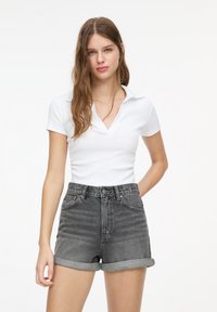 White short-sleeve polo shirt with a V-neck; paired with high-waisted gray denim shorts, rolled cuffs, and subtle fading details.