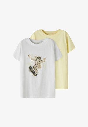 Dwie koszulki z krótkim rękawem i okrągłym dekoltem, jedna biała z grafiką deskorolkarza, druga jednolita w bladożółtym kolorze, przedstawione na białym tle, częściowo nałożone na siebie.