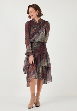 Long-sleeve, patterned dress in dark hues with ruffled hemline. Sheer fabric, cinched waist, and high neckline. Paired with beige ankle boots.