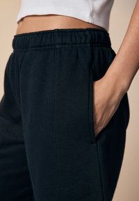 Schwarze Jogginghose seitlich gezeigt, mit elastischem Bund und Seitentaschen, gefertigt aus einem weichen, strukturierten Stoff.