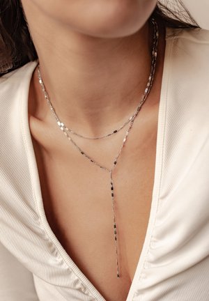 Die silberne, mehrschichtige Halskette besteht aus dünnen, zarten Ketten mit einem strukturierten Design. Eine Kette bildet einen Lariat-Stil und fällt elegant herab.