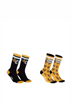 Deux paires de chaussettes mi-mollet : une noire avec des orteils et talons jaunes ornée d'un design d'œil ailé, l'autre jaune avec des orteils, talons et motifs de logos noirs.