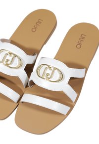 Hvide slide-sandaler med to vandrette remme, pyntet med en guld, cirkulær spænde-detail, hvilende på en tan polstret sål.