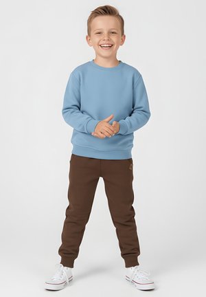 Jasnoniebieska bluza z okrągłym dekoltem, zestawiona z brązowymi spodnimi dresowymi. Białe trampki z czerwonymi akcentami. Gładka tekstura, luźne dopasowanie.