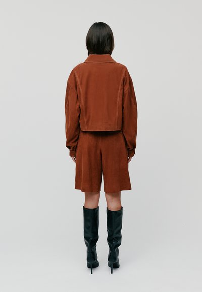 Braune Wildlederjacke und Shorts-Set, das ein kurzes Design aufweist, mit langen Ärmeln und knielangen Shorts. Schwarze kniehohe High-Heels-Stiefel.