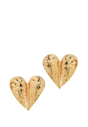 Paire de boucles d'oreilles en forme de cœur brillantes en or martelé, avec un pli central et des marques noires légèrement irrégulières sur un fond blanc.