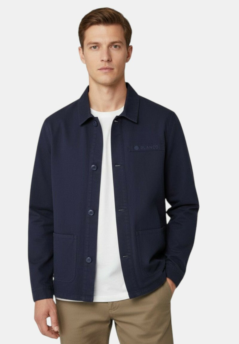 Veste bleu marine à boutons, confectionnée dans un tissu lisse avec un col structuré, deux poches avant et un petit logo sur la poitrine.