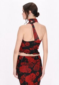 Schwarzes Blumen-Haltertop mit rotem Rosenmuster. Hat eine figurschmeichelnde Silhouette, einen rüschengeschmückten Saum und ein offenes Rückendesign.