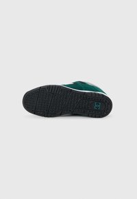 Schwarze Gummisohle eines Sneakers mit strukturiertem Traktionsmuster, ausgestattet mit grünen und grauen Akzenten auf einem Wildleder-Obermaterial und weißen Details.