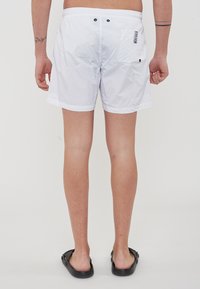 Shorts da nuoto bianchi con elastico in vita, chiusura a bottone e tasche laterali. Presenta una toppa con logo sulla tasca destra.