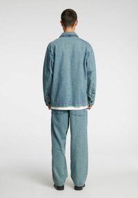 Svetlo modra denim jakna in ujemajoče se široke hlače z udobnim krojem, vidnimi šivi in velikimi zadnjimi žepi. Preprosta bela majica.