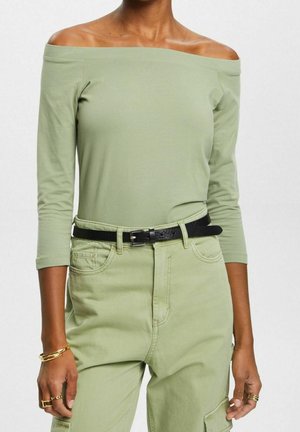 Lichtgroene off-the-shoulder top met lange mouwen, gecombineerd met hoog-waisted lichtgroene broek, geaccentueerd met een zwarte riem. Soepele katoenstructuur.