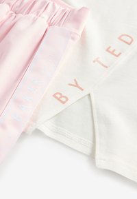 Banda elastică de culoare roz deschis cu textură adunată și un material alb cu un logo imprimat în auriu roz. Amestec moale și ușor de bumbac.