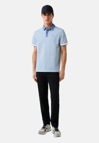 Gestreepte polo-shirt met korte mouwen in lichtblauw en donkerblauw, met een placket met twee knopen en een contrasterende kraag, gecombineerd met zwarte broek en sneakers.