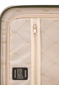 Interior de una maleta verde que presenta una tela beige con un patrón de logo repetido, compartimentos con cremallera y un bolsillo de malla para organización.