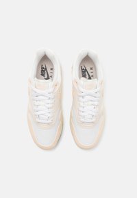 Nike Air sporta apavi baltā un maigi persiku krāsā. Iespējas ietver tīkla un sintētisko augšdaļu, apaļās šnerves, mīkstu apkakli un mīkstinātu zoli.