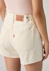 Shorts en denim blanc à taille haute, avec une étiquette tissée à l'arrière, cinq poches, et une texture lisse.