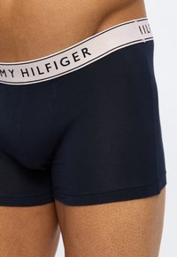 Κοντινό πλάνο ενός ατόμου που φοράει μποξέρ Tommy Hilfiger σε ναυτικό μπλε χρώμα με διάτρητη ελαστική μέση που φέρει το εμπορικό σήμα.